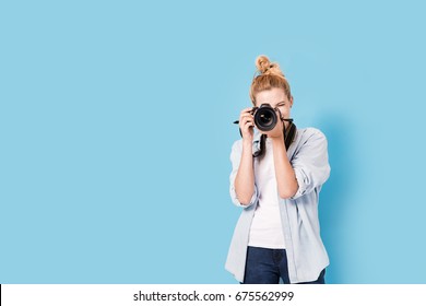 Young blonde photographer is taking a photo. Model isolated on a blue background with copy space