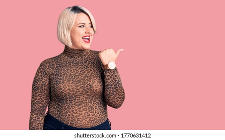 Young blonde plus size woman wearing casual leopard t-shirt smiling with happy face looking and pointing to the side with thumb up.  - Shutterstock ID 1770631412