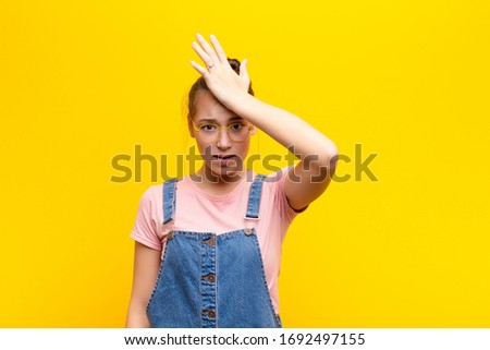 young blonde pretty girl raising palm to forehead thinking oops, after making a stupid mistake or remembering, feeling dumb against yellow wall