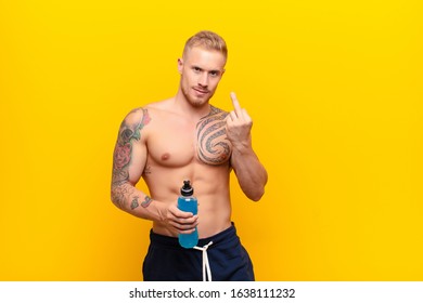 Young Blonde Strong Man Feeling Angry, Annoyed, Rebellious And Aggressive, Flipping The Middle Finger, Fighting Back With An Energy Drink