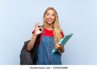 Young blonde student woman over isolated blue wall showing an ok sign with fingers - Shutterstock ID 1500018488