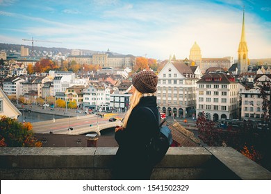 Young blonde tourist girl in warm hat and coat with backpack walking at cold autumn in Europe city enjoying her travel in Zurich Switzerland - tourism holiday background