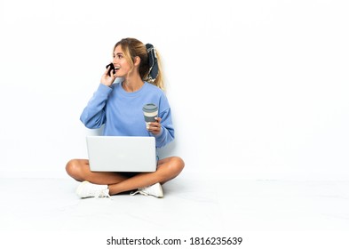 Young Blonde Uruguayan Girl With The Laptop Isolated On White Background Holding Coffee To Take Away And A Mobile