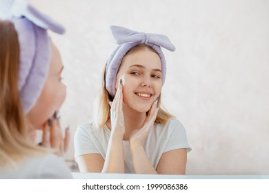 Young Blonde Woman Applies Facial Cleaner For Skin Wash. Teen Girl Washing Face In Morning In Bathroom. Self Care Morning Bathroom Routine Woman Portrait Reflection In Mirror.
