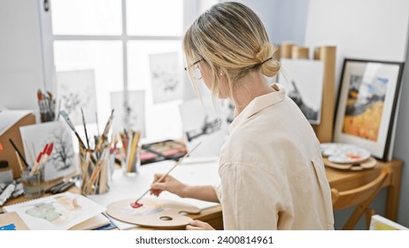 Young blonde woman artist drawing on paper sitting on table at art studio - Powered by Shutterstock