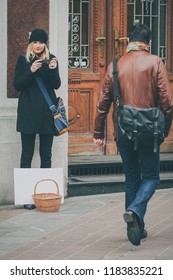 Young Blonde Woman Begging For Money With An Accordeon And A Blank White Signboard And A Basket, While People Are Rushing Past Her.