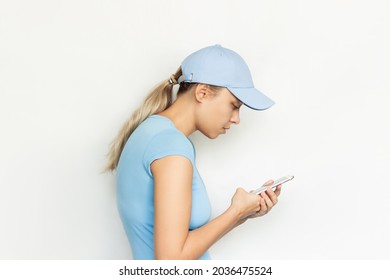 A young blonde woman in a blue cap with a hunched back looks at the mobile phone screen isolated on a white background. Incorrect back position, curvature of posture, spine. Dependence on gadgets