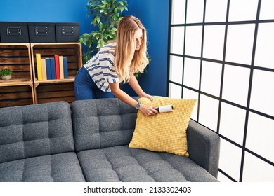 Young Blonde Woman Cleaning Sofa Using Pet Hair Roller At Home