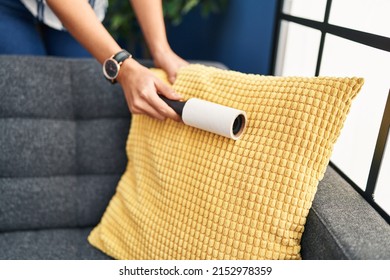 Young Blonde Woman Cleaning Sofa Using Pet Hair Roller At Home