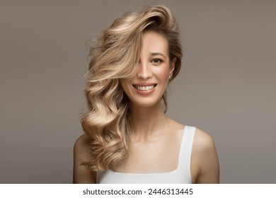 young blonde woman with curly beautiful hair smiles on a gray background - Powered by Shutterstock