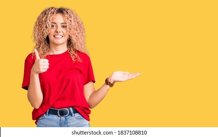 Young Blonde Woman With Curly Hair Wearing Casual Red Tshirt Showing Palm Hand And Doing Ok Gesture With Thumbs Up, Smiling Happy And Cheerful 