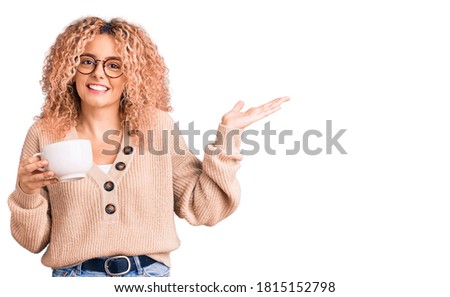 Young blonde woman with curly hair wearing glasses and drinking a cup of coffee celebrating victory with happy smile and winner expression with raised hands 