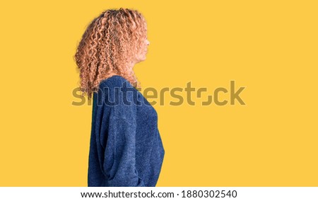 Young blonde woman with curly hair wearing casual winter sweater looking to side, relax profile pose with natural face and confident smile. 