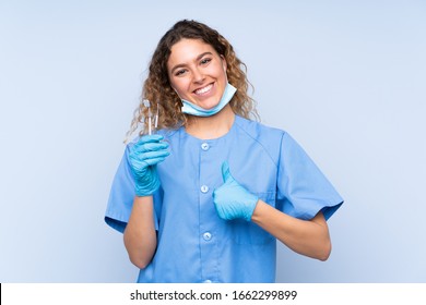 Young Blonde Woman Dentist Holding Tools Isolated On Blue Background Giving A Thumbs Up Gesture