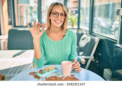 Young blonde woman drinking coffee and eating french macaron sitting at the terrace.