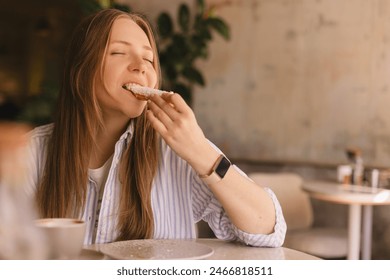 Young blonde woman eating eclair sitting in cafe. Girl bite piece of croissant look joyful at restaurant. Cheat meal day concept. Woman is preparing with appetite to eat eclair. Enjoy coconut bakery. - Powered by Shutterstock