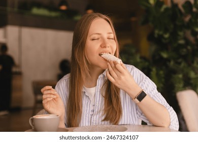 Young blonde woman eating eclair sitting in cafe. Girl bite piece of croissant look joyful at restaurant. Cheat meal day concept. Woman is preparing with appetite to eat eclair. Enjoy coconut bakery. - Powered by Shutterstock