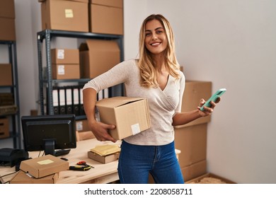 Young blonde woman ecommerce business worker using smartphone holding package at office - Powered by Shutterstock