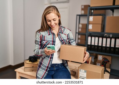 Young blonde woman ecommerce business worker using smartphone holding package at office