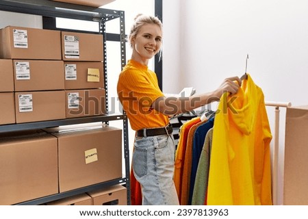 Young blonde woman ecommerce business worker organizing clothes on coat rack at office