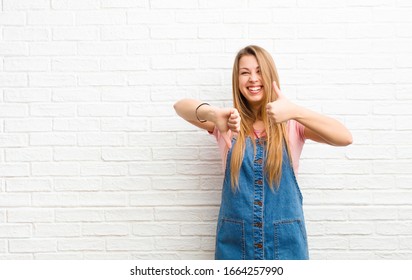 Young Blonde Woman Feeling Confused, Clueless And Unsure, Weighting The Good And Bad In Different Options Or Choices Against Brick Wall