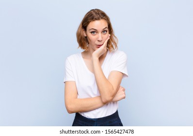 young blonde woman feeling shocked and astonished holding face to hand in disbelief with mouth wide open against flat color wall - Shutterstock ID 1565427478