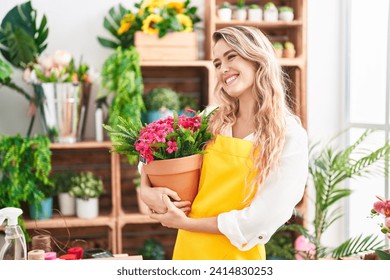 Young blonde woman florist smiling confident holding plant at florist - Powered by Shutterstock