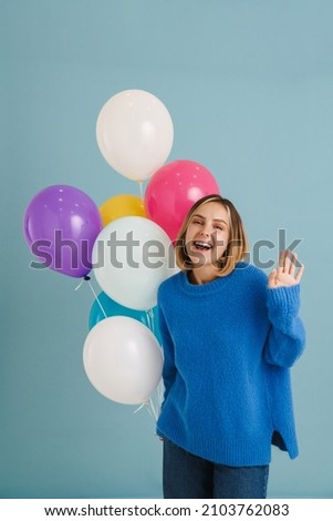 Young blonde woman gesturing while posing with balloons isolated over blue background