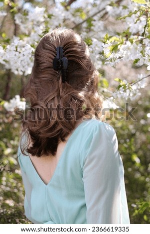 Young blonde woman with her back to camera showcasing claw clip hairstyle. Half-up claw clip style. Spring hairstyle. Trendy hairstyle. Black plastic claw clip.