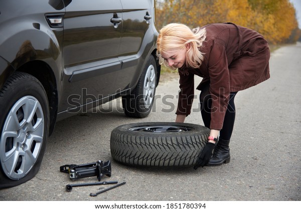 A young blonde woman hold spare tire
near her car with a flat tire, trouble on the
road.