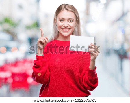 Young blonde woman holding blank paper card over isolated background surprised with an idea or question pointing finger with happy face, number one