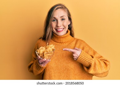 Young blonde woman holding bowl with uncooked pasta smiling happy pointing with hand and finger 
