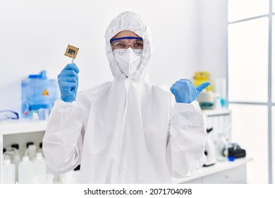 Young Blonde Woman Holding Cpu Computer Processor At Laboratory Pointing Thumb Up To The Side Smiling Happy With Open Mouth 