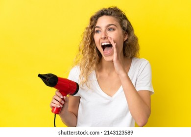 Young Blonde Woman Holding A Hairdryer Isolated On Yellow Background Shouting With Mouth Wide Open To The Side