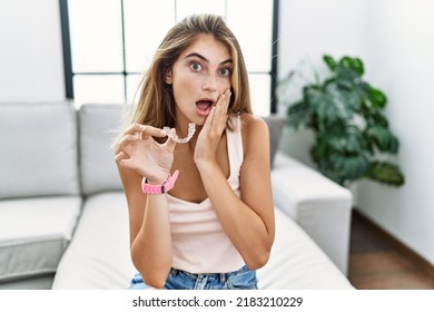 Young blonde woman holding invisible aligner orthodontic afraid and shocked, surprise and amazed expression with hands on face 