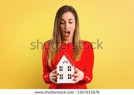 Young blonde woman holding a little house on yellow background