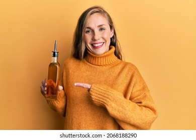 Young blonde woman holding olive oil can smiling happy pointing with hand and finger 