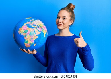 Young Blonde Woman Holding World Ball Smiling Happy And Positive, Thumb Up Doing Excellent And Approval Sign 