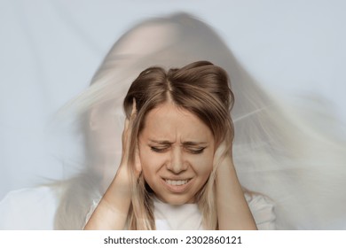 Young blonde woman holds her head and covers her ears with her hands. The girl doesn't want to hear the noise. Voices in the head. Headache. Schizophrenia, split personality, depression, obsession