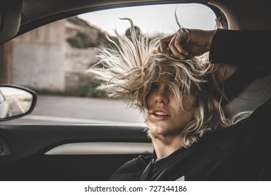 Young blonde woman inside a car with the window open and her hair at the wind