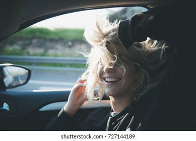 Young Blonde Woman Inside A Car With The Window Open And Her Hair At The Wind