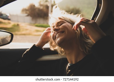 Young Blonde Woman Inside A Car With The Window Open And Her Hair At The Wind