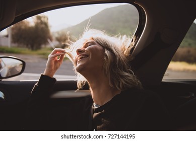 Young Blonde Woman Inside A Car With The Window Open And Her Hair At The Wind