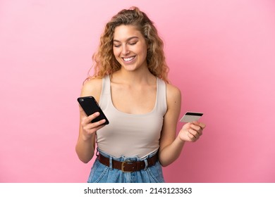 Young Blonde Woman Isolated On Pink Background Buying With The Mobile With A Credit Card