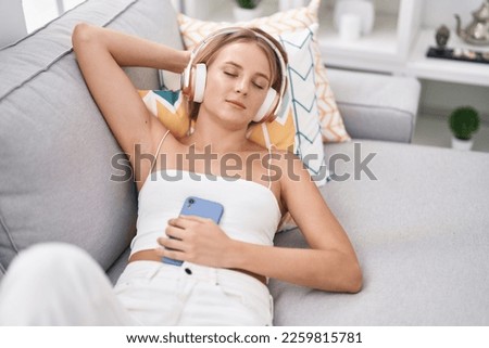 Young blonde woman listening to music relaxed on sofa at home