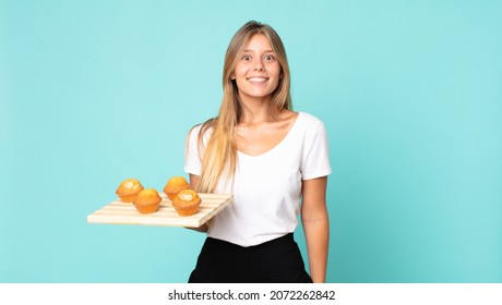 Young Blonde Woman Looking Happy And Pleasantly Surprised And Holding A Muffins Troy