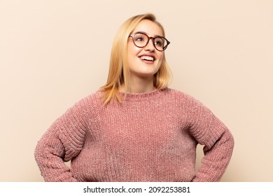 Young Blonde Woman Looking Happy, Cheerful And Confident, Smiling Proudly And Looking To Side With Both Hands On Hips