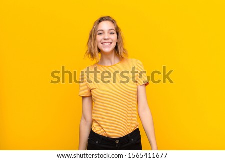 young blonde woman looking happy and goofy with a broad, fun, loony smile and eyes wide open against flat color wall
