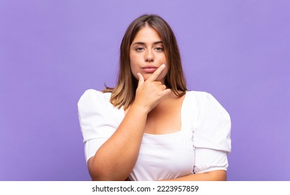 Young Blonde Woman Looking Serious, Thoughtful And Distrustful, With One Arm Crossed And Hand On Chin, Weighting Options