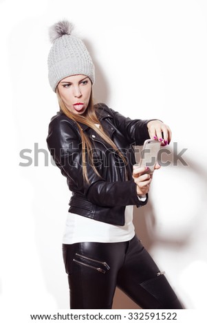 young blonde woman making faces and gestures,taking selfie with smart phone, studio white